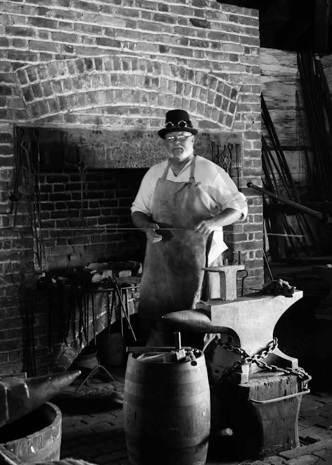 Black & white photograph of a Blacksmith at the forge at Fort George, Niagara-on-the-Lake, for sale as fine art by Sage & Balm
