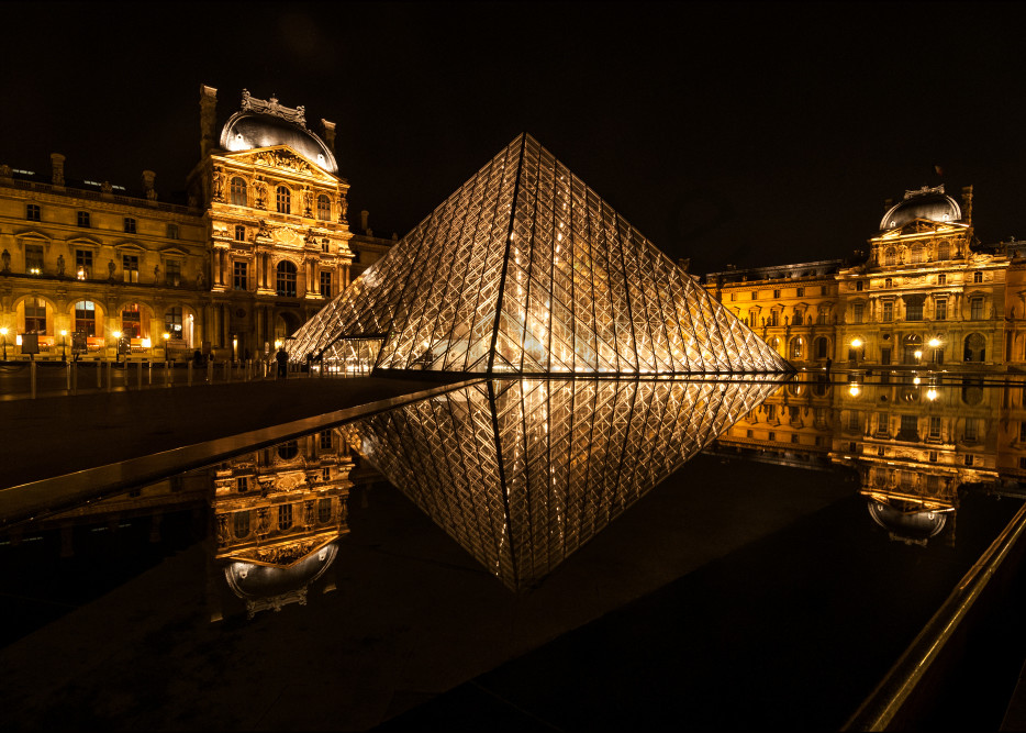 photograph of the louvre art museum at night reflecting in still water.