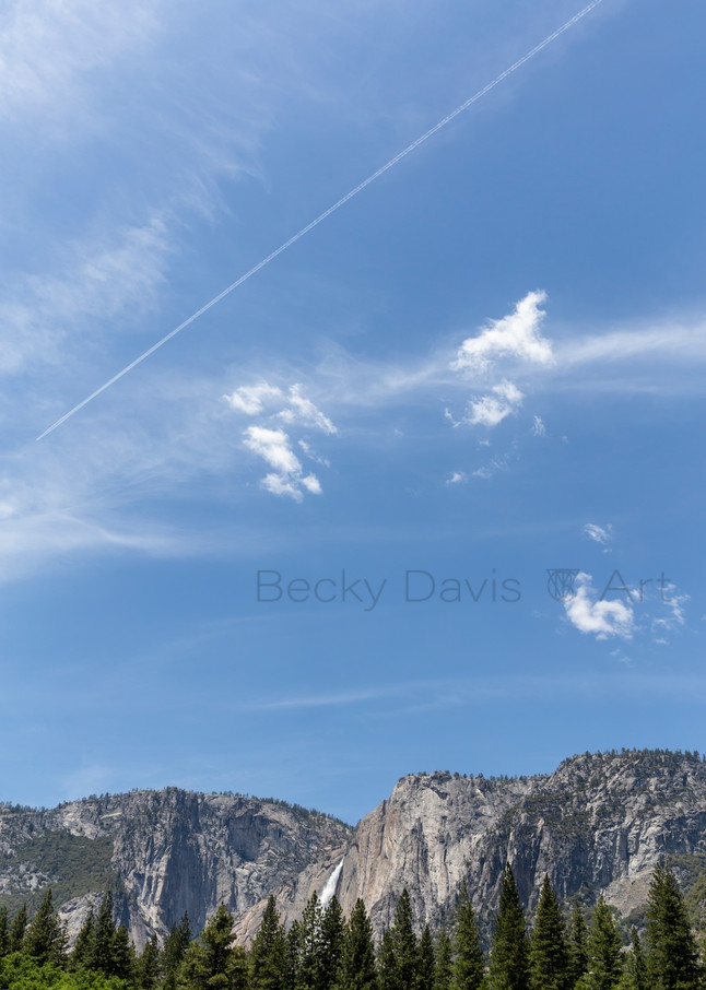 Blue sky and white clouds fill a vertical frame of Yosemite Falls.