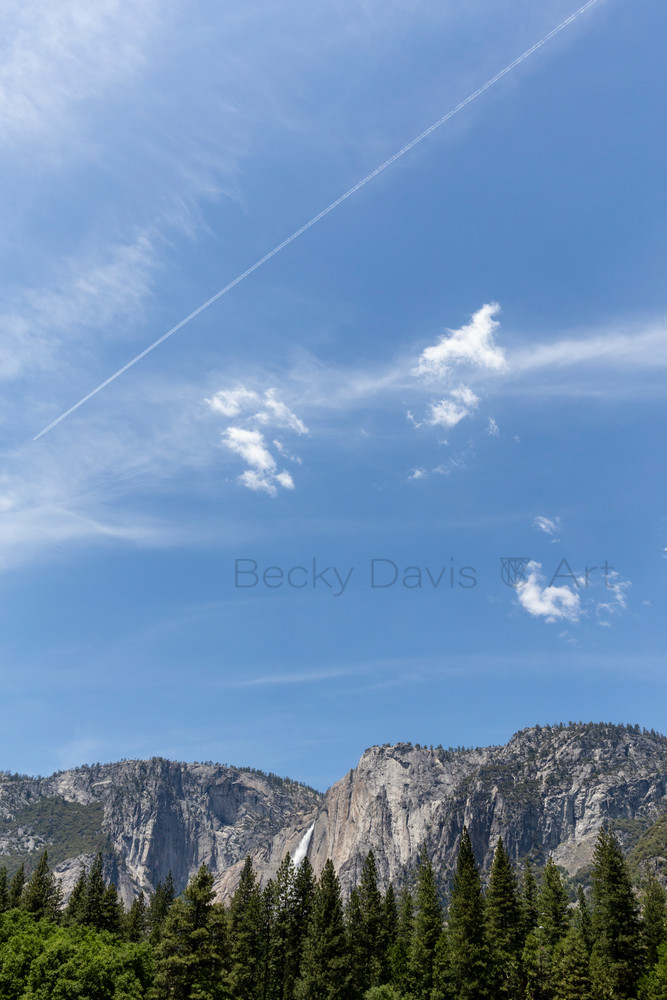 Blue sky and white clouds fill a vertical frame of Yosemite Falls.