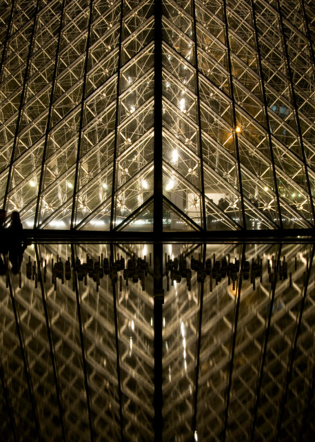 Photograph of silhouetted couple by louvre art museum at night with reflection in water