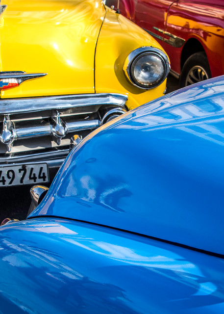 Fine art photograph of red, yellow and blue classic cars inHavana, with reflection on hood