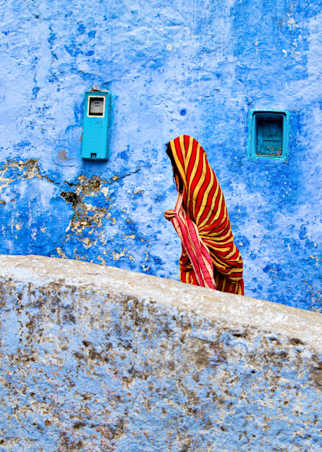 Travel photograph of woman in bright red and yellow chador walking in front of blue wall in Chefchaouan Morocco the blue city