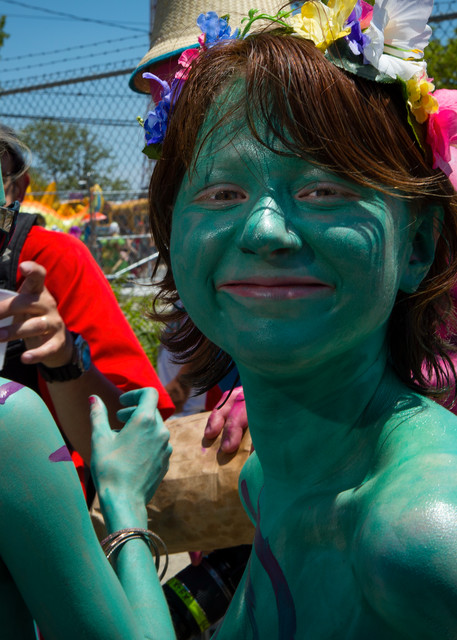 A woman smiles as a friend gets the finishing touches of body paint applied prior to the start of the annual; Mermaid Parade in Coney Island.