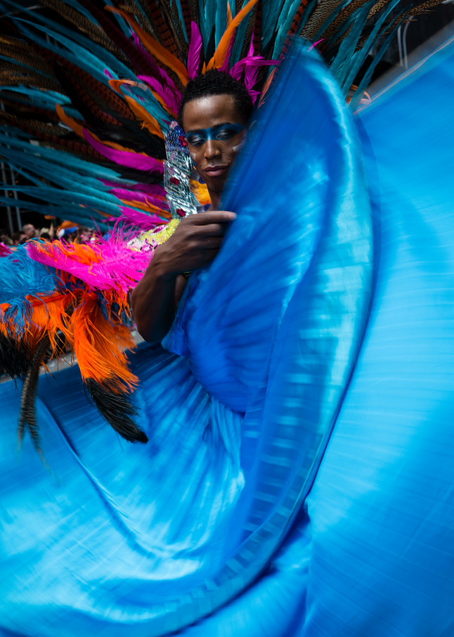 A man in a large feathered headdress waves his turquoise cape.