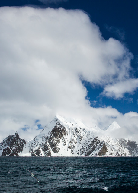 Mountainous snowy island with dark blue ocean swells and sky with billowing clouds
