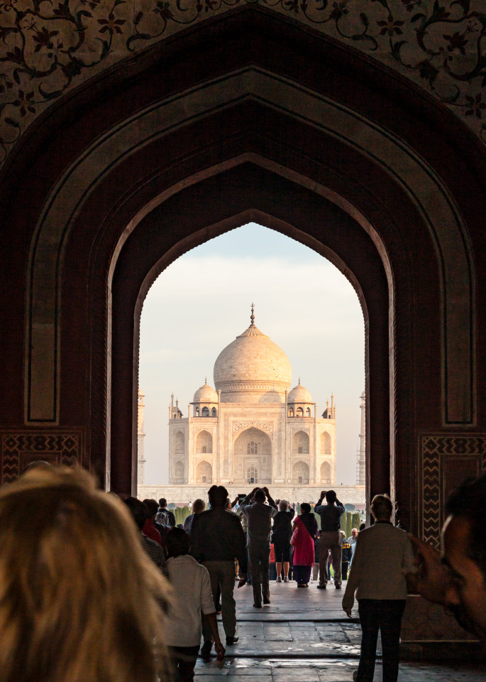 Looking through the main entrance gate at The Taj Mahal in Agra, India with tourists taking pictures in the foreground.