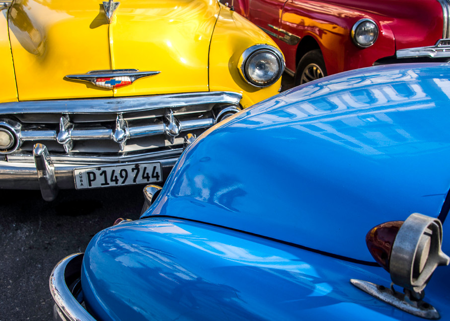 Fine art photograph of red, yellow and blue classic cars inHavana, with reflection on hood