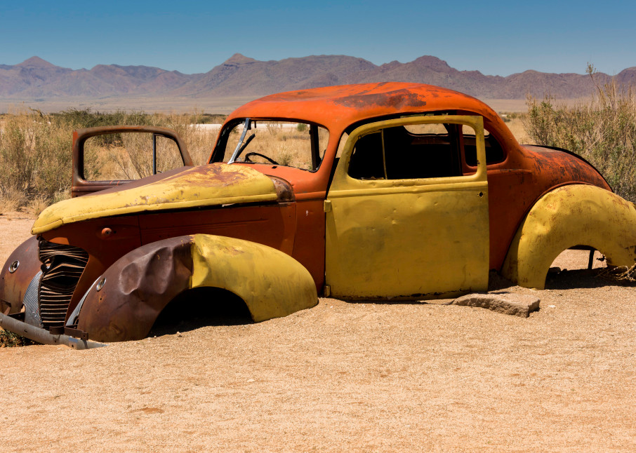 A yellow, orange and brown shell of a car in the desert, in art photograph