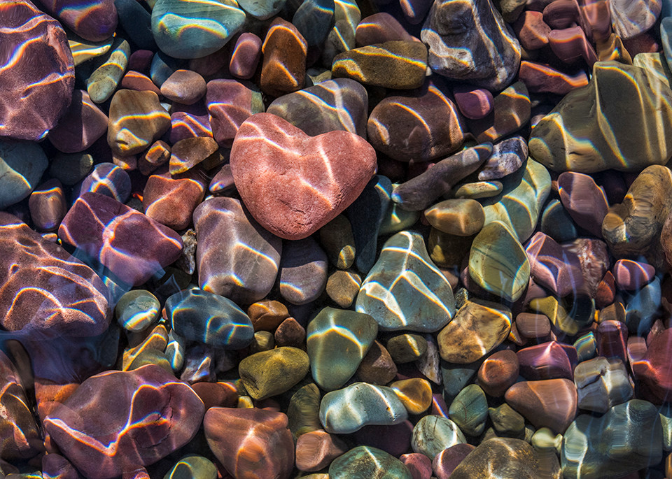 Touching heart shape rock amidst colorful stones in lake