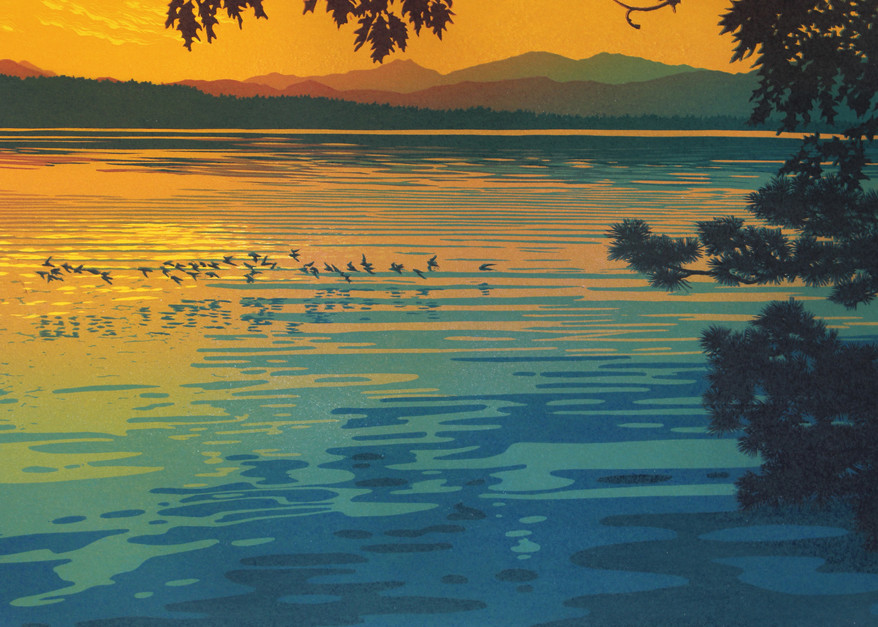 Birds skim the surface of a lake at sunset.