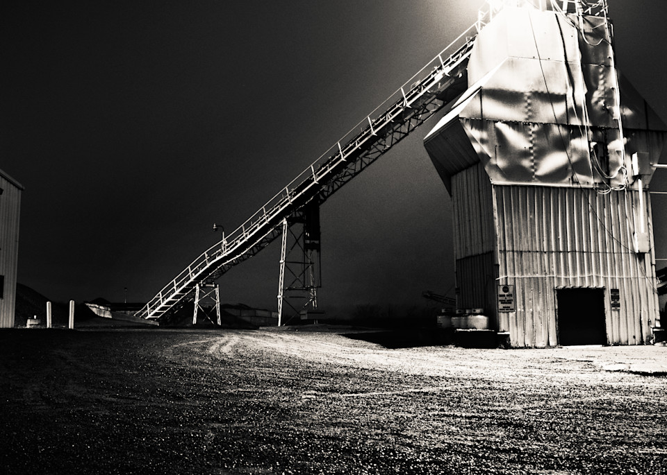 Night photo of an industrial mill with light shining from the top.