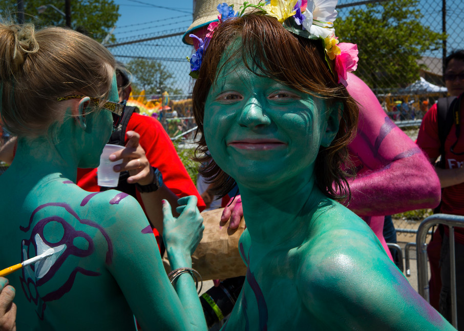 A woman smiles as a friend gets the finishing touches of body paint applied prior to the start of the annual; Mermaid Parade in Coney Island.