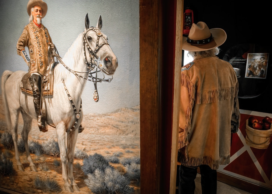 A Buffalo Bill impersanator walks past a Buffalo Bill painting