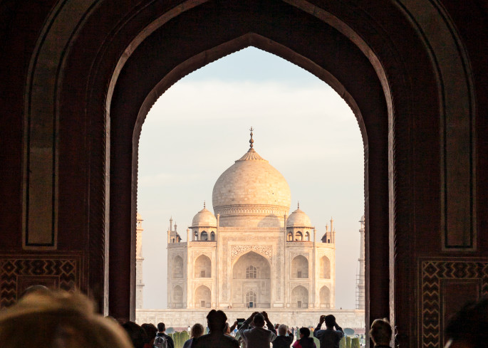 Looking through the main entrance gate at The Taj Mahal in Agra, India with tourists taking pictures in the foreground.