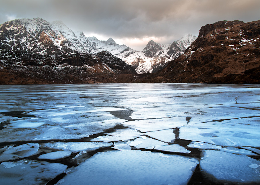 The sun breaks through for just a moment on a moody winter day in the Lofoten Archipelago over an icy lake, norway