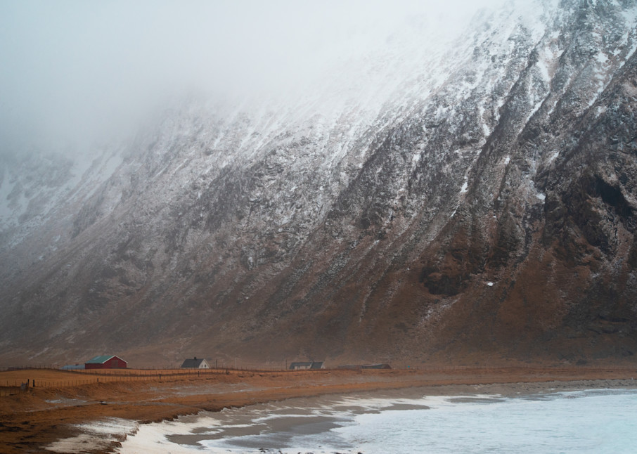 The mountains of the fjord tower next to the rural homes as the clouds descend toward the ground -- Lofoten, Norway