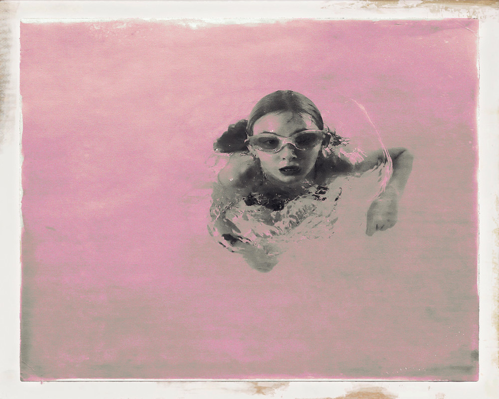 Photograph of adolescent girl swimming in pink water.  