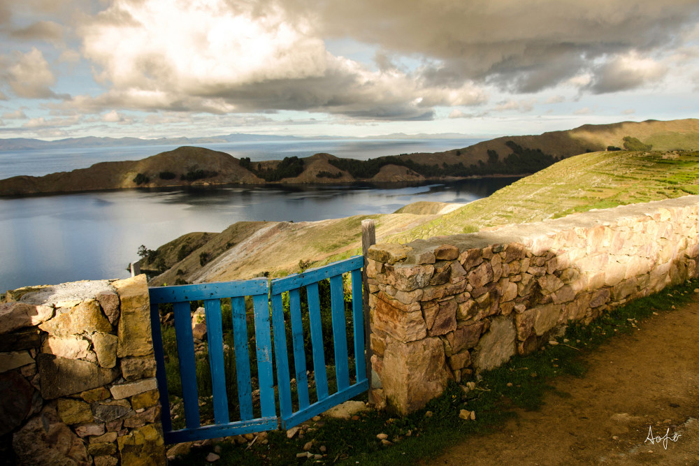 Fine art photograph of blue gate on Inca wall with fields and water behind