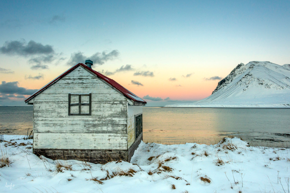 Rustic winter cabin by lake and snowy mountain in a fine art photograph print.
