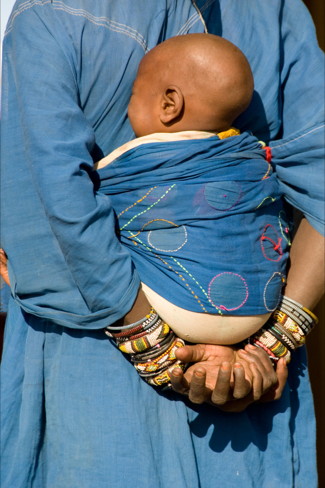 Fine art photograph of mother holding baby on her back with colorful bracelets