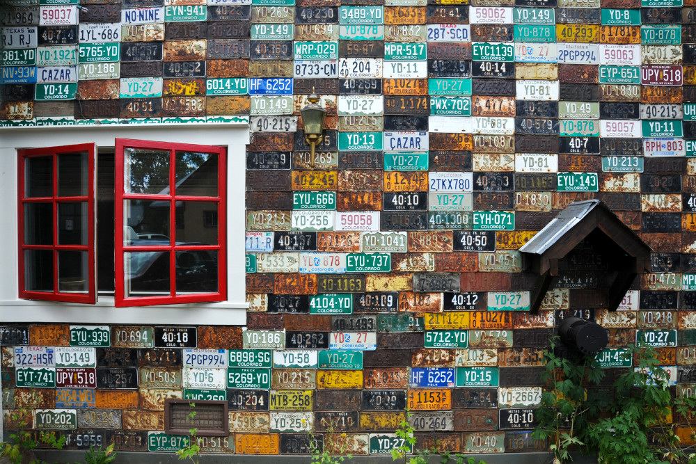 Art house covered in license plates with red window, in photograph print