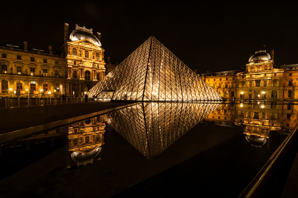 photograph of the louvre art museum at night reflecting in still water.
