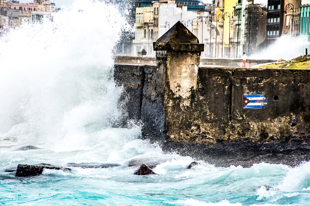 A man stands on the Malecon with waves crashing around him in a powerful  art photograph