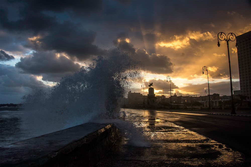 Wave crashing over Malecon at sunrise, with rays coming from clouds, in a fine art photograph