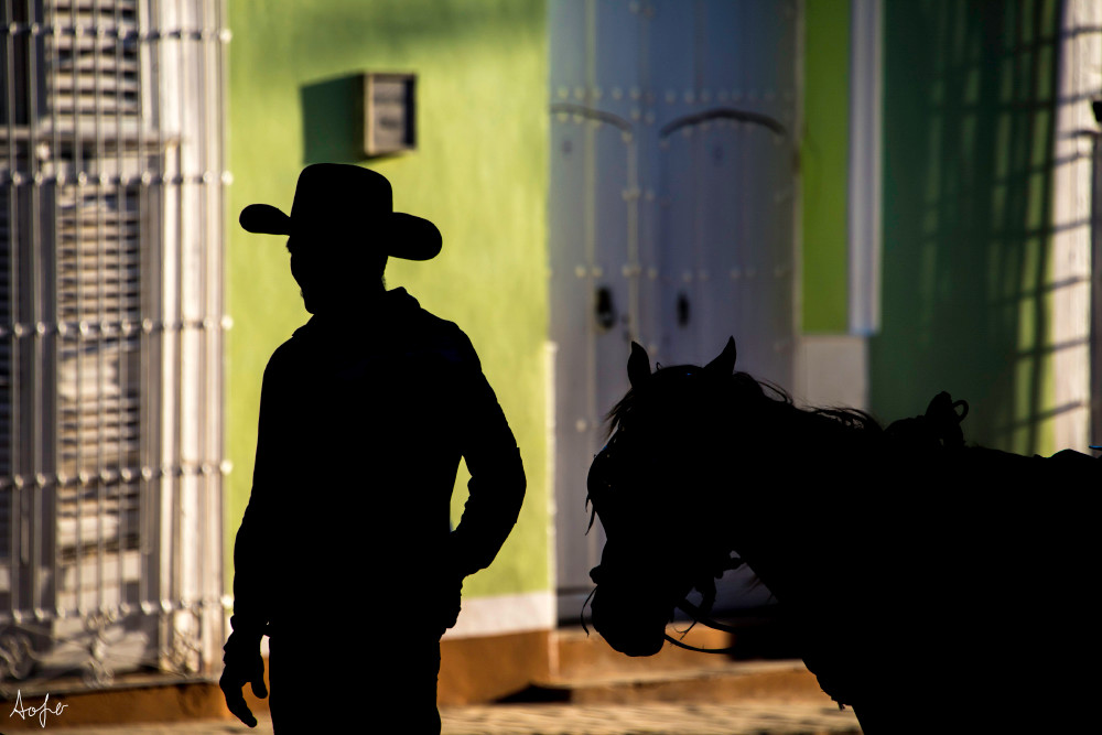Silhouette of cowboy leading his horse with colorful houses behind in an art photograph
