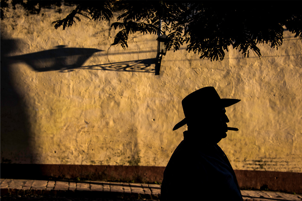 Fine art photograph of a silhouette of man in cowboy hat with cigar in mouth by mustard wall