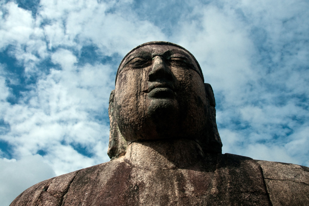 Weathered Buddha statue with blue sky and white clouds above, in art photograph print