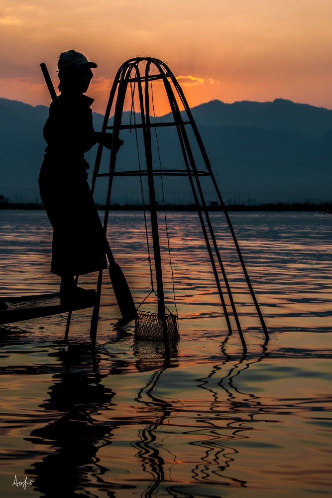 Foot rower in silhouette lifting fish trap at sunrise, in fine art photograph