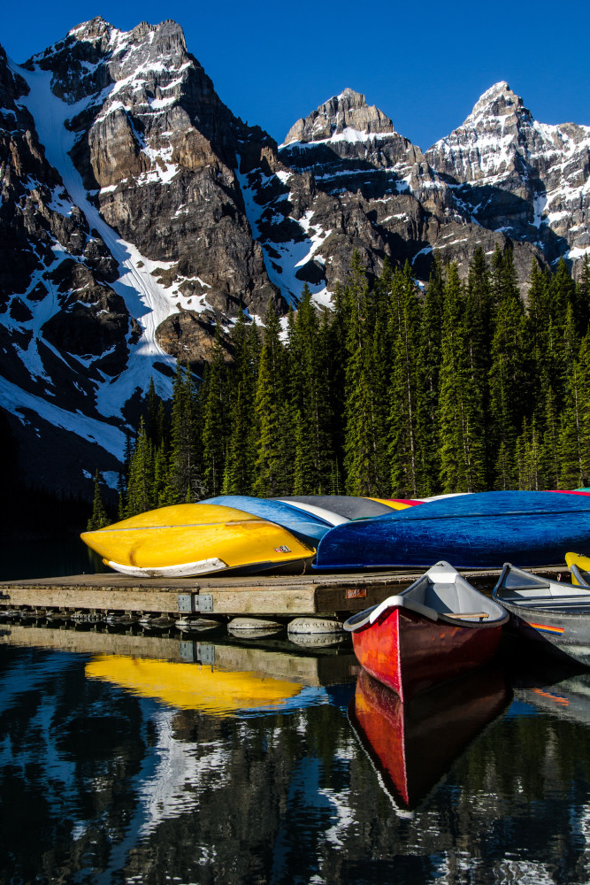 Colorful canoes on Moraine Lake with snow capped peaks.