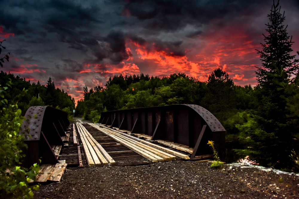 An old iron bridge with a fiery sunset sky, and dark clouds, fine art photograph