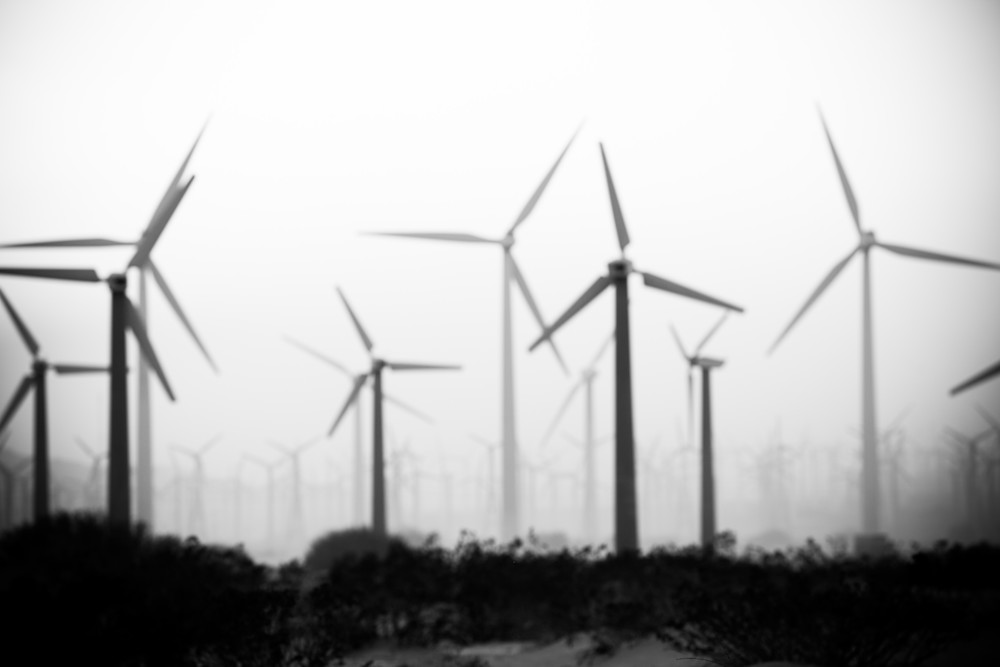 black and white of windmills in midst of fog.