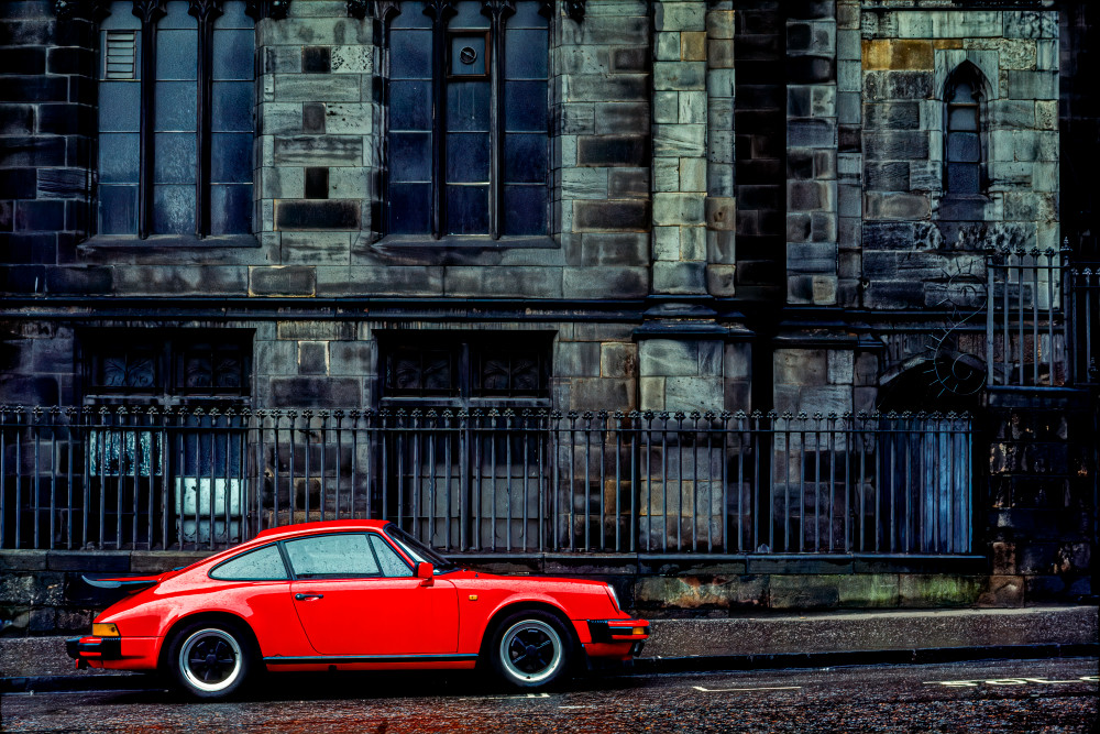 A red Porche 911, in front of centuries old grey  stone structure,  Edinburgh, Scotland