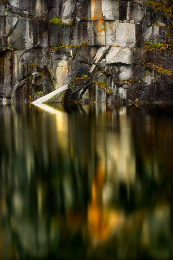Reflections of stone quarry in stillness of pond