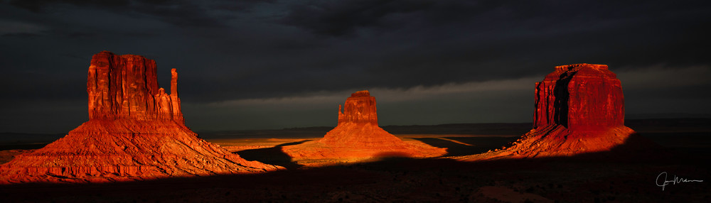 Monument Valley during a great sunset with dark clouds enhancing the Mittens.