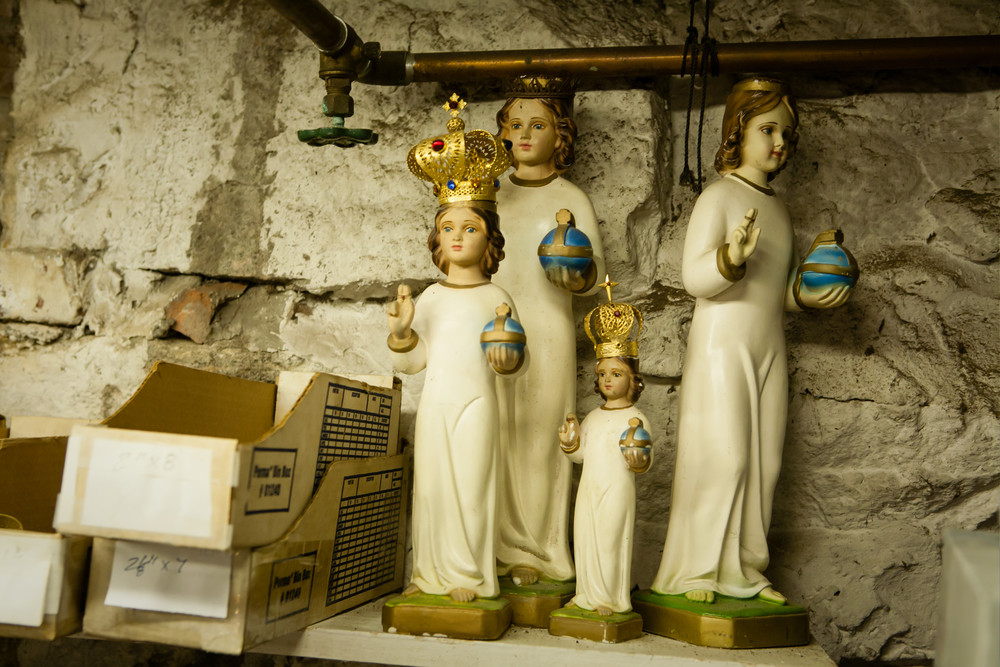 A group of small religious statues, some with crowns, in Martin's workshop. he statues are commonly supplied with simple robes coast as part of the statue; fabric robes are added later.