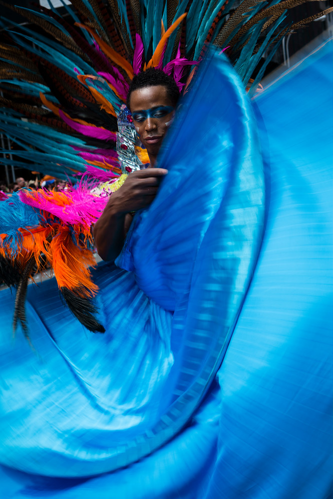 A man in a large feathered headdress waves his turquoise cape.