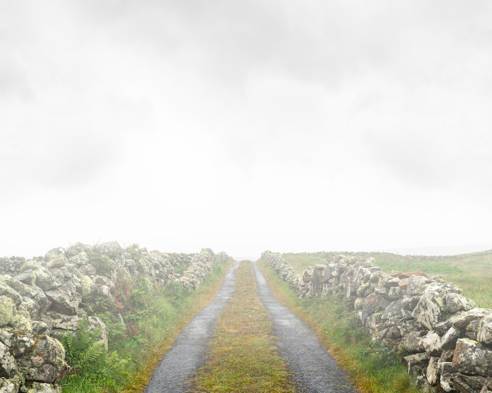 A stone wall lined dirt road covered in fog in county connemara Ireland by Mia DelCasino