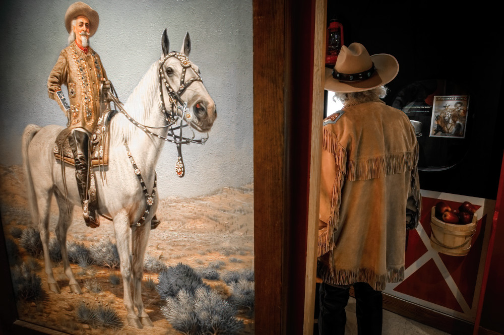 A Buffalo Bill impersanator walks past a Buffalo Bill painting