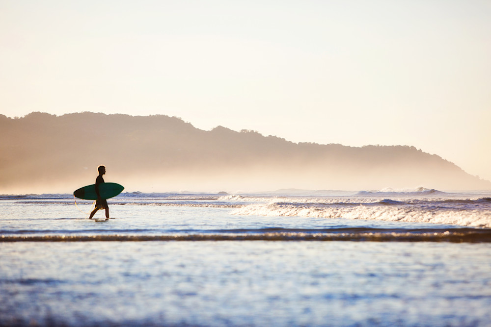 A surfer sets out to surf the Costa Rica waves at sunrise by fine art photographer Allison Davis