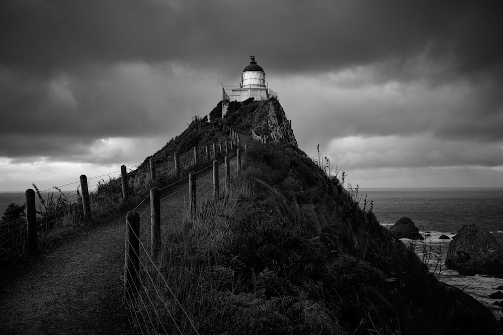 Monochrome fine art photograph of a moody lighthouse on a point.