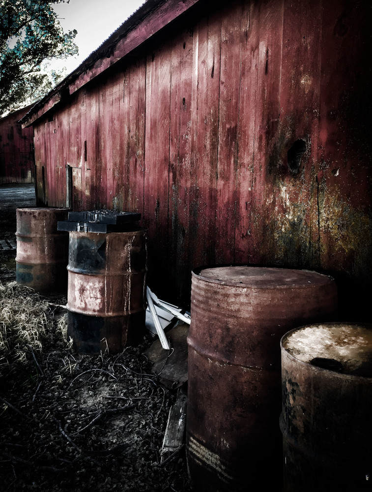 Aging barrels line the weather-beaten side of a farm shed.