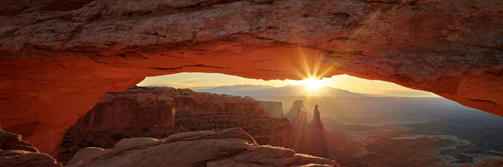 A vivid landscape photograph of a sunburst through a natural stone arch