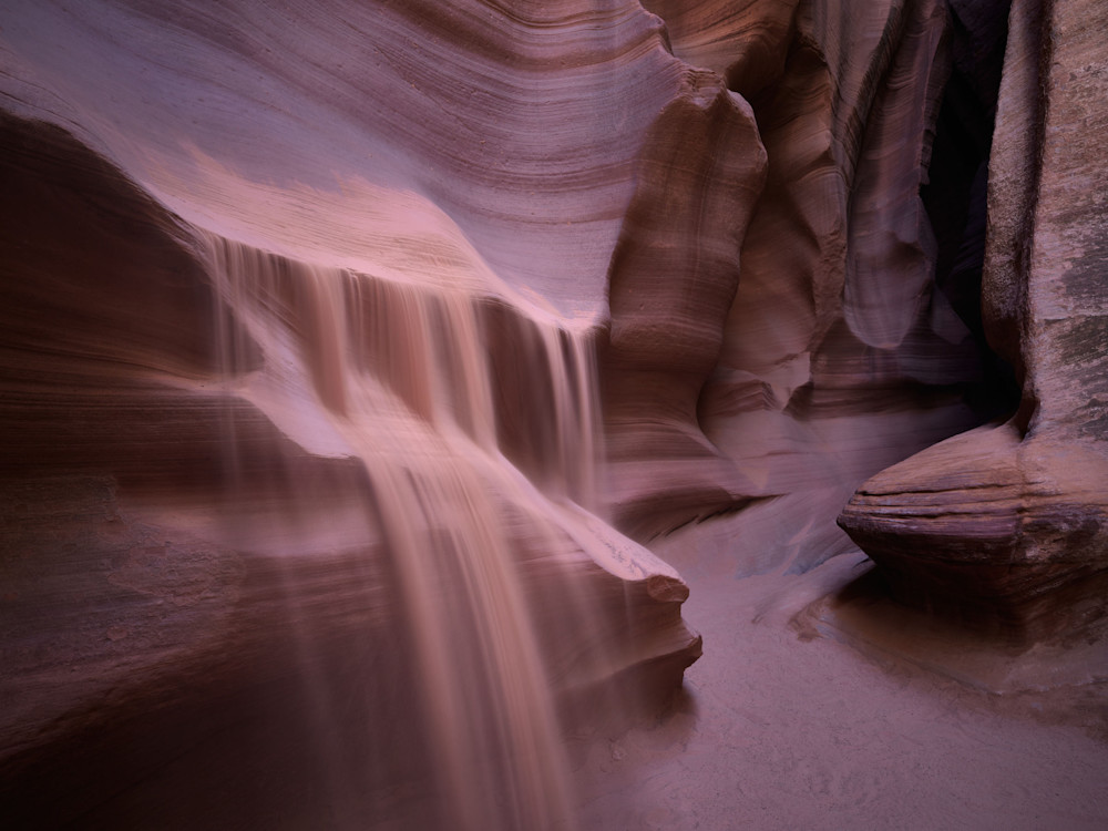 A dreamlike photograph of sand spilling from a ledge in a slot canyon.