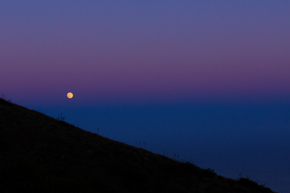 Golden moon rising over a blue sunset in malibu