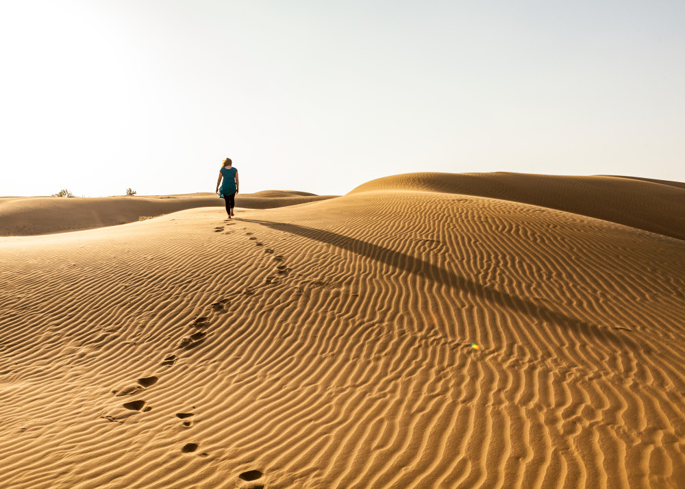 A woman walking on the sand dunes in the Thar Desert, Rajasthan, India. Near Rawala Resort.